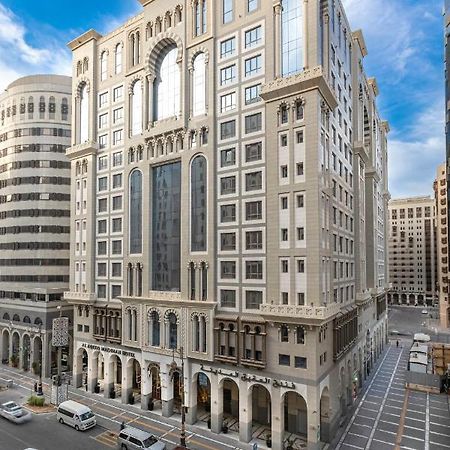 Al Aqeeq Madinah Hotel Medina Exterior photo The photo depicts a large, modern building with a distinctive architectural style. The structure shows a blend of classic and contemporary design elements, featuring ornate details, large glass windows, and a prominent central facade. Surrounding the