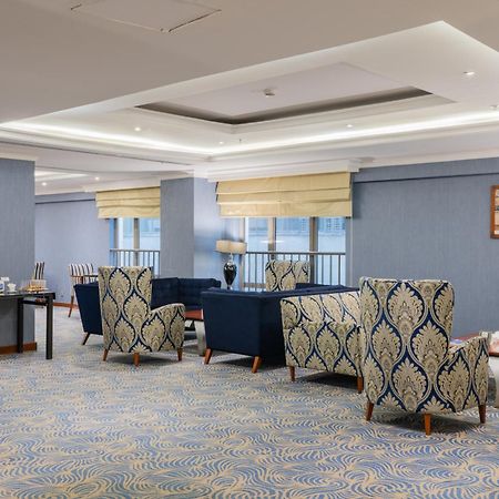 Al Aqeeq Madinah Hotel Medina Exterior photo The photo shows a stylish indoor lounge or sitting area. It features several upholstered armchairs arranged around a central space. The chairs have a blue and cream patterned upholstery, creating a sophisticated ambiance. There is a table alongside s