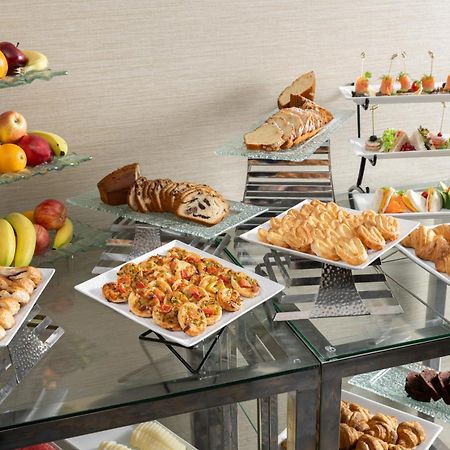 Al Aqeeq Madinah Hotel Medina Exterior photo The photo showcases a buffet-style spread featuring a variety of food items. There are several platters with appetizers, including seafood dishes, pastries, and other savory items. In addition, there is a selection of fresh fruit displayed on a glass