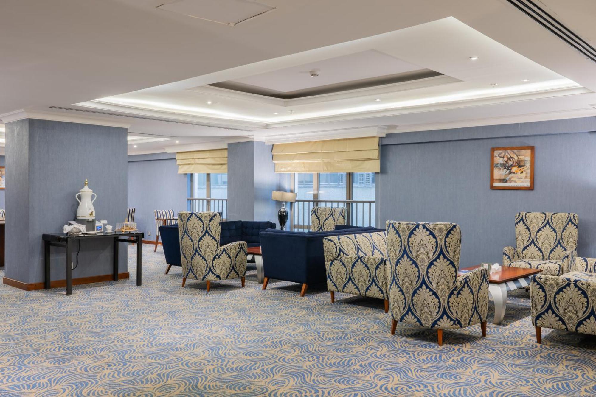 Al Aqeeq Madinah Hotel Medina Exterior photo The photo shows a stylish indoor lounge or sitting area. It features several upholstered armchairs arranged around a central space. The chairs have a blue and cream patterned upholstery, creating a sophisticated ambiance. There is a table alongside s