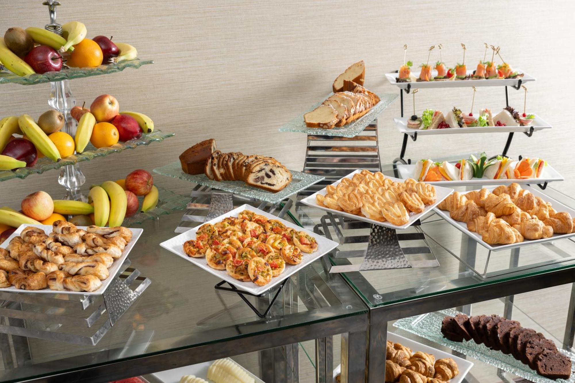 Al Aqeeq Madinah Hotel Medina Exterior photo The photo showcases a buffet-style spread featuring a variety of food items. There are several platters with appetizers, including seafood dishes, pastries, and other savory items. In addition, there is a selection of fresh fruit displayed on a glass