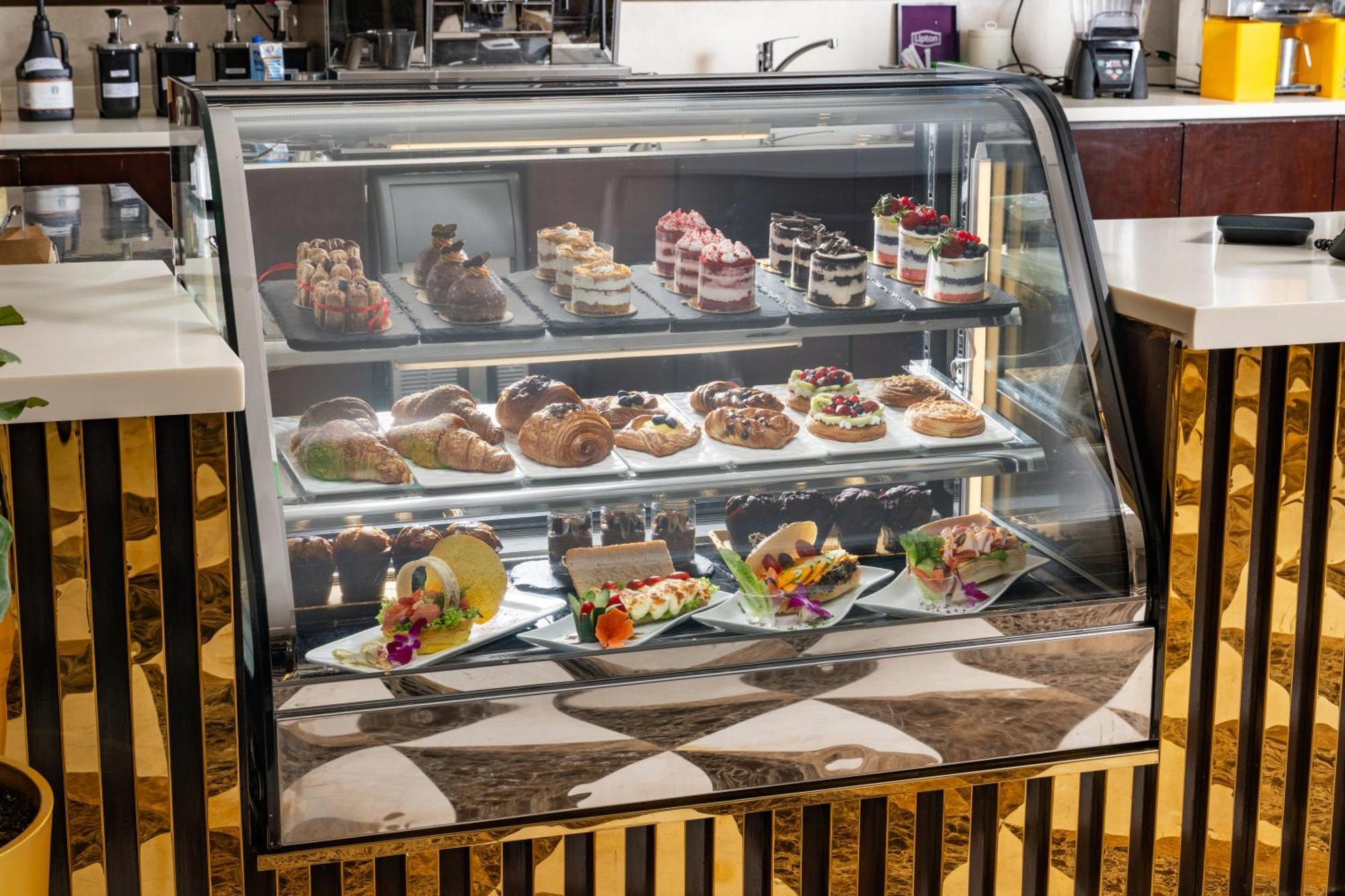 Al Aqeeq Madinah Hotel Medina Exterior photo The photo shows a display case filled with an assortment of desserts. There are various types of pastries, including cakes, tarts, and croissants, arranged neatly on different shelves. The desserts are visually appealing, with colorful decorations, f
