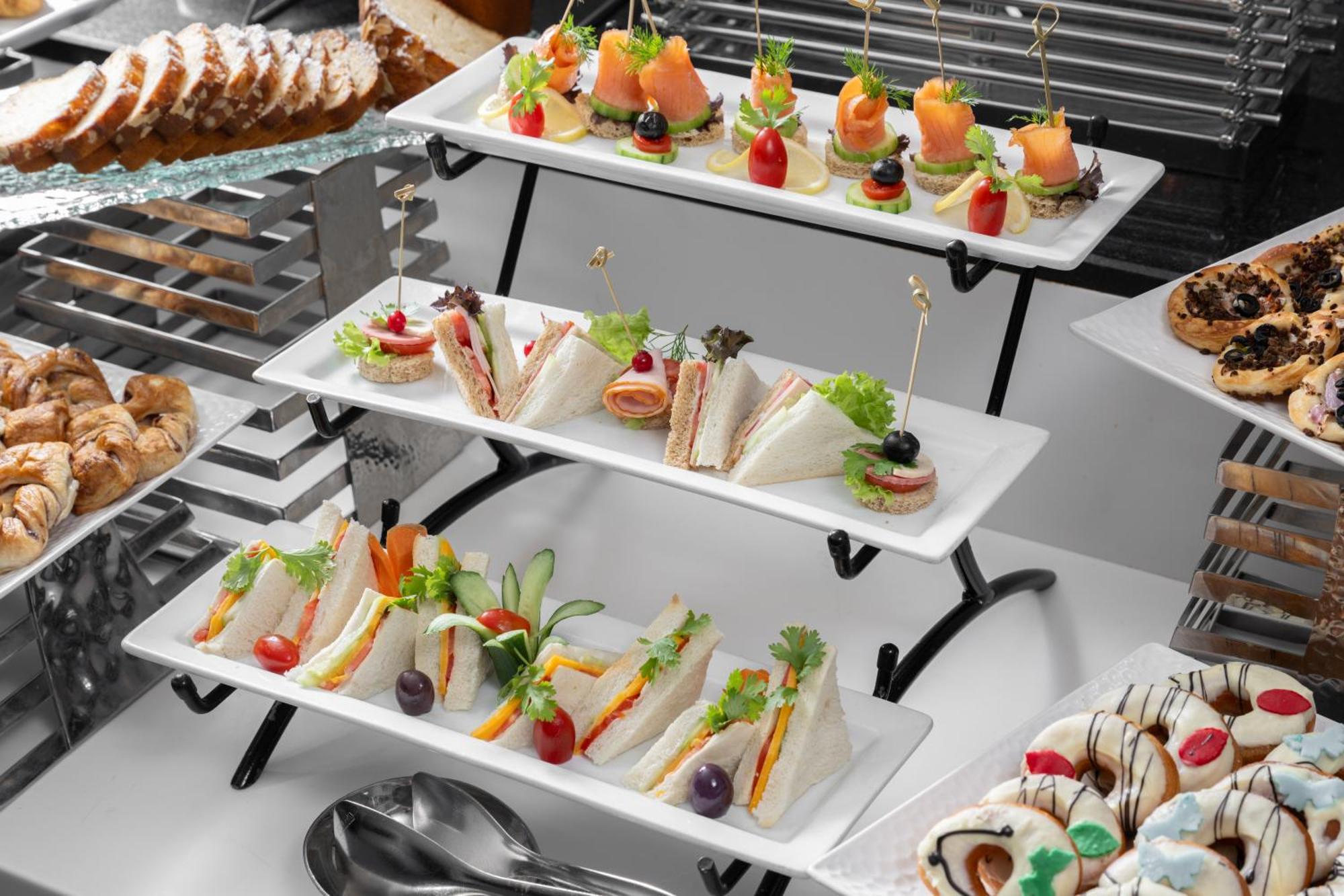 Al Aqeeq Madinah Hotel Medina Exterior photo The photo shows a tiered display of assorted appetizers and snacks arranged on white rectangular plates. 

1. **Top Tier**: Contains small bites featuring smoked salmon garnished with greenery, and some with colorful cherry tomatoes on toothpicks. 

