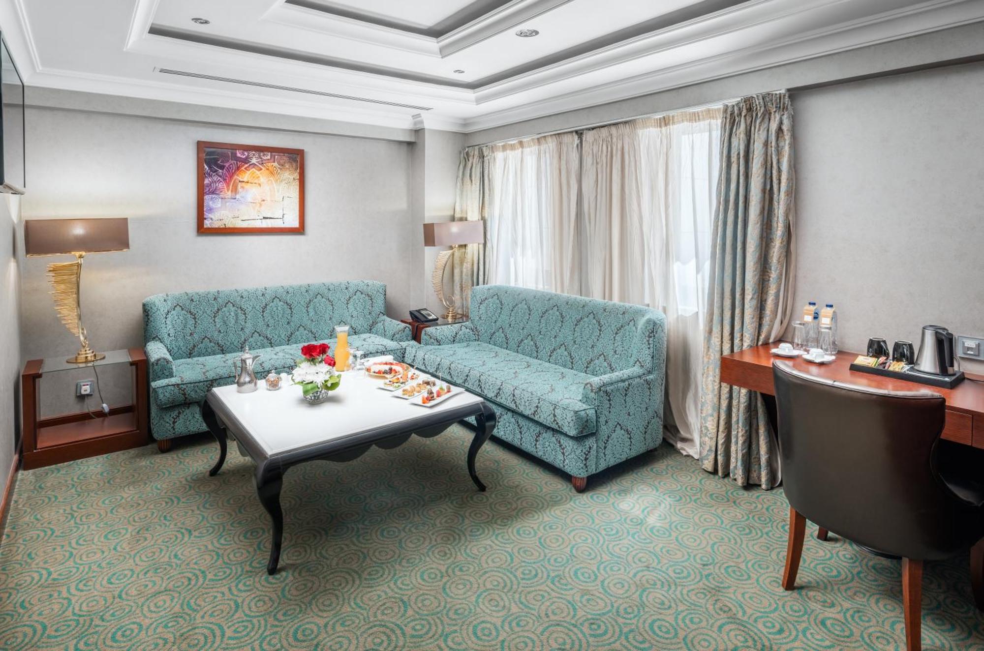Al Aqeeq Madinah Hotel Medina Exterior photo The photo shows a cozy hotel room or lounge area. It features two light blue sofas arranged around a low coffee table. On the table, there are snacks or refreshments arranged aesthetically. The room has a neutral color palette with a textured carpet 