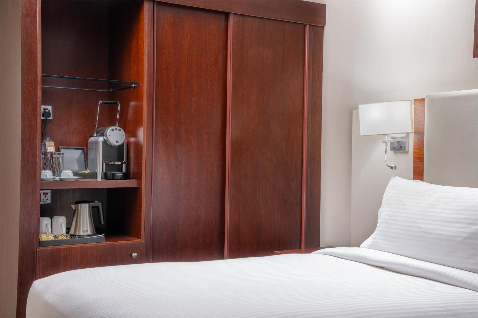 Al Aqeeq Madinah Hotel Medina Exterior photo The photo shows a hotel room with a minimalist design. On the left side, there's a wooden cabinet with sliding doors that houses a small coffee maker and additional amenities, such as cups and a kettle. The bed is neatly made with white bedding and i