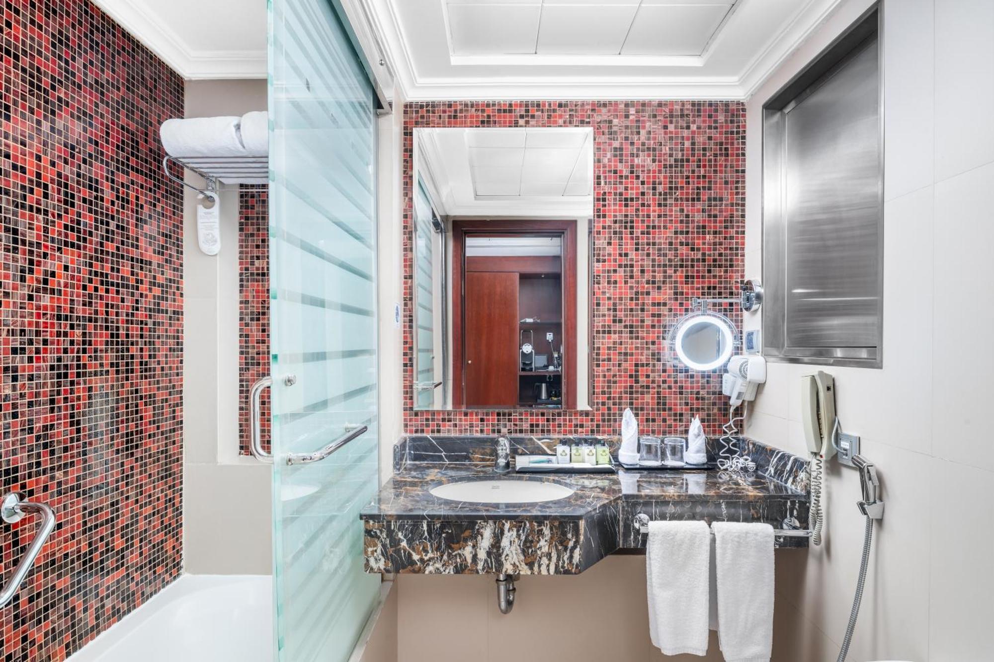 Al Aqeeq Madinah Hotel Medina Exterior photo The photo shows a modern bathroom featuring a mix of design elements. The walls have a vibrant red mosaic tile pattern, adding a bold touch to the space. There is a glass shower enclosure, and next to it, a sleek countertop with a dark, marbled surfa