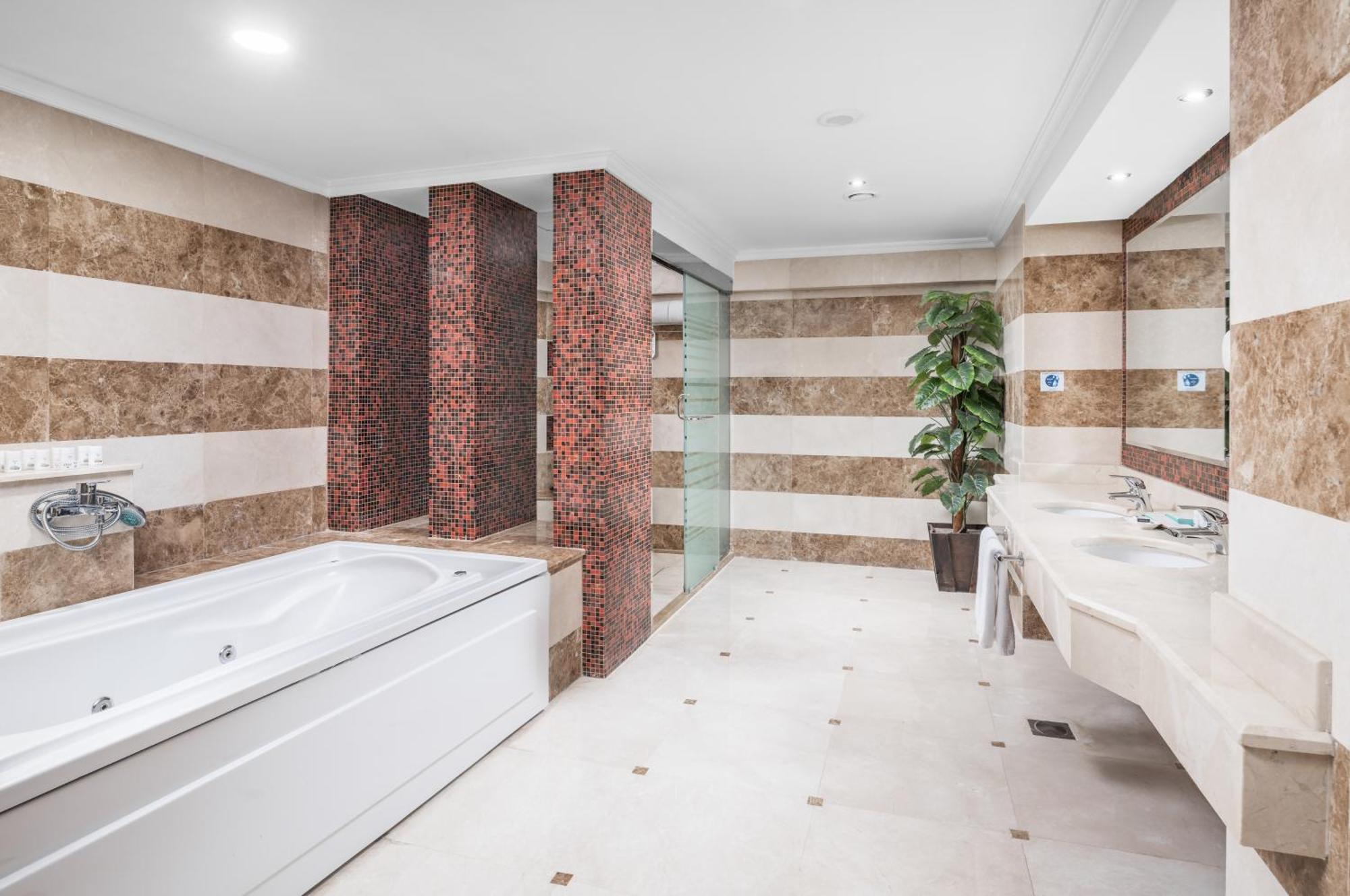 Al Aqeeq Madinah Hotel Medina Exterior photo The photo shows a modern bathroom featuring a spacious layout. On one side, there is a large, white bathtub adjacent to a textured wall with warm, earthy tones. The walls are decorated with alternating horizontal stripes of light and dark colors. 

I