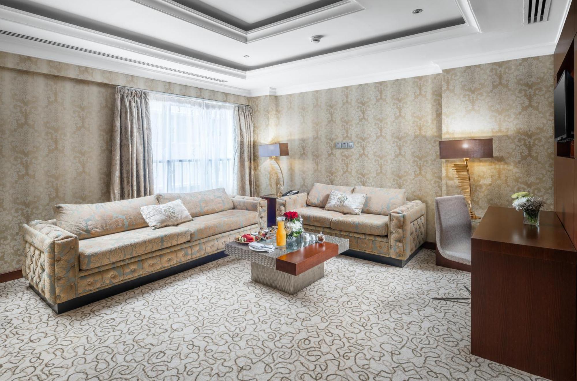 Al Aqeeq Madinah Hotel Medina Exterior photo The photo shows a stylish living room with an elegant design. There are two beige sofas placed opposite each other, adorned with decorative pillows. A low coffee table is positioned in the center, featuring various items, possibly drinks or decorativ