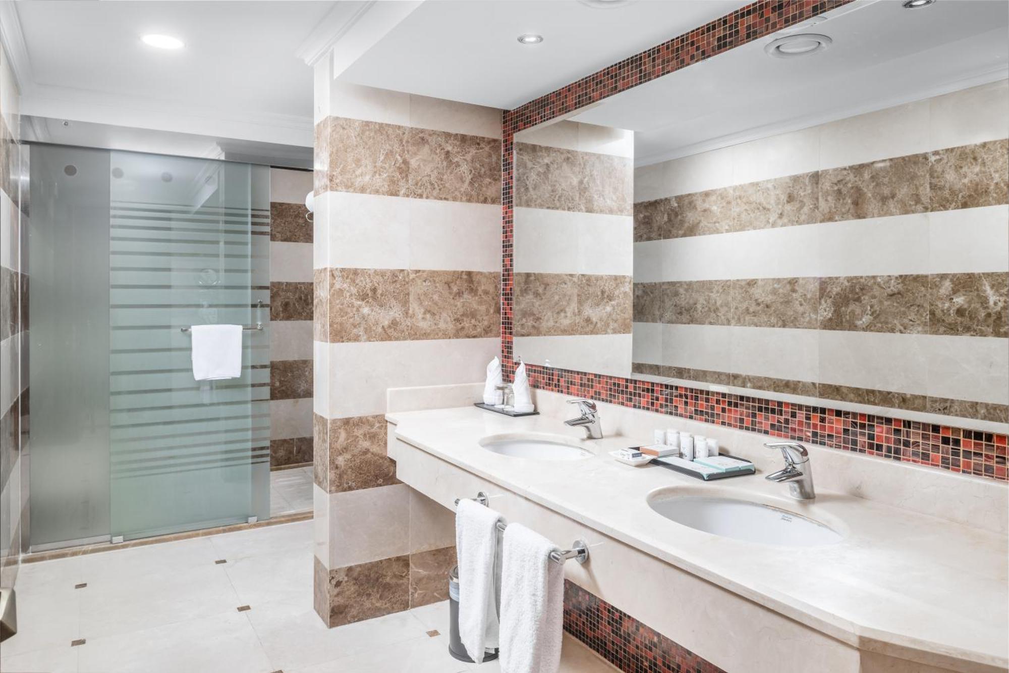 Al Aqeeq Madinah Hotel Medina Exterior photo The photo shows a modern bathroom with an elegant design. It features a large double sink with a smooth countertop, accompanied by faucets. The walls are adorned with alternating horizontal stripes of light and dark materials, creating a stylish look