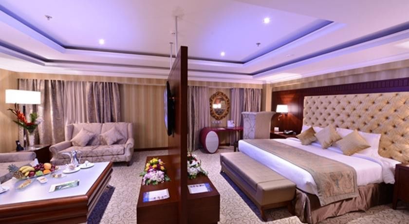 Al Aqeeq Madinah Hotel Medina Exterior photo The image shows a luxurious hotel room. It features a large bed with a tufted headboard, flanked by nightstands with lamps. There's a seating area with a plush sofa and a coffee table. A decorative partition separates the bed from the living area. Th