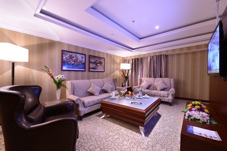 Al Aqeeq Madinah Hotel Medina Exterior photo The photo shows a stylish and comfortable living room. It features two light-colored sofas with decorative cushions arranged around a modern coffee table. In one corner, there's a dark, leather armchair. The walls are adorned with framed artwork, and