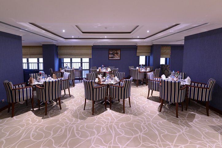 Al Aqeeq Madinah Hotel Medina Exterior photo The photo shows an elegant dining room equipped with several tables. Each table is set with white tableware and neatly arranged silverware, giving a formal dining appearance. The decor features striped chairs and a carpet with a subtle pattern. The w