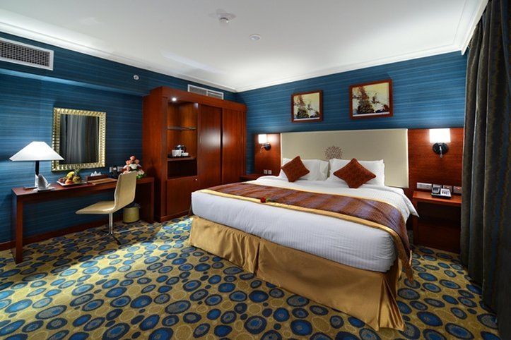Al Aqeeq Madinah Hotel Medina Exterior photo The photo shows a hotel room designed with a modern and stylish aesthetic. It features a large bed with a cream-colored headboard and decorative pillows. The room is decorated with blue walls and patterned carpet, creating a cozy atmosphere. 

There 