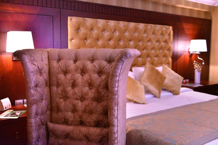 Al Aqeeq Madinah Hotel Medina Exterior photo The image shows a luxurious bedroom featuring a large upholstered headboard with a tufted design in a soft, beige color. The bed is elegantly dressed with decorative pillows and a textured bedspread. In the background, there are wooden paneling and s