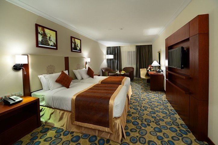 Al Aqeeq Madinah Hotel Medina Exterior photo The photo shows a hotel room featuring two beds with white linens and brown throw blankets. There are decorative pillows on the beds. The room has a modern design, with wooden furniture including bedside tables and a large wooden unit that houses a t